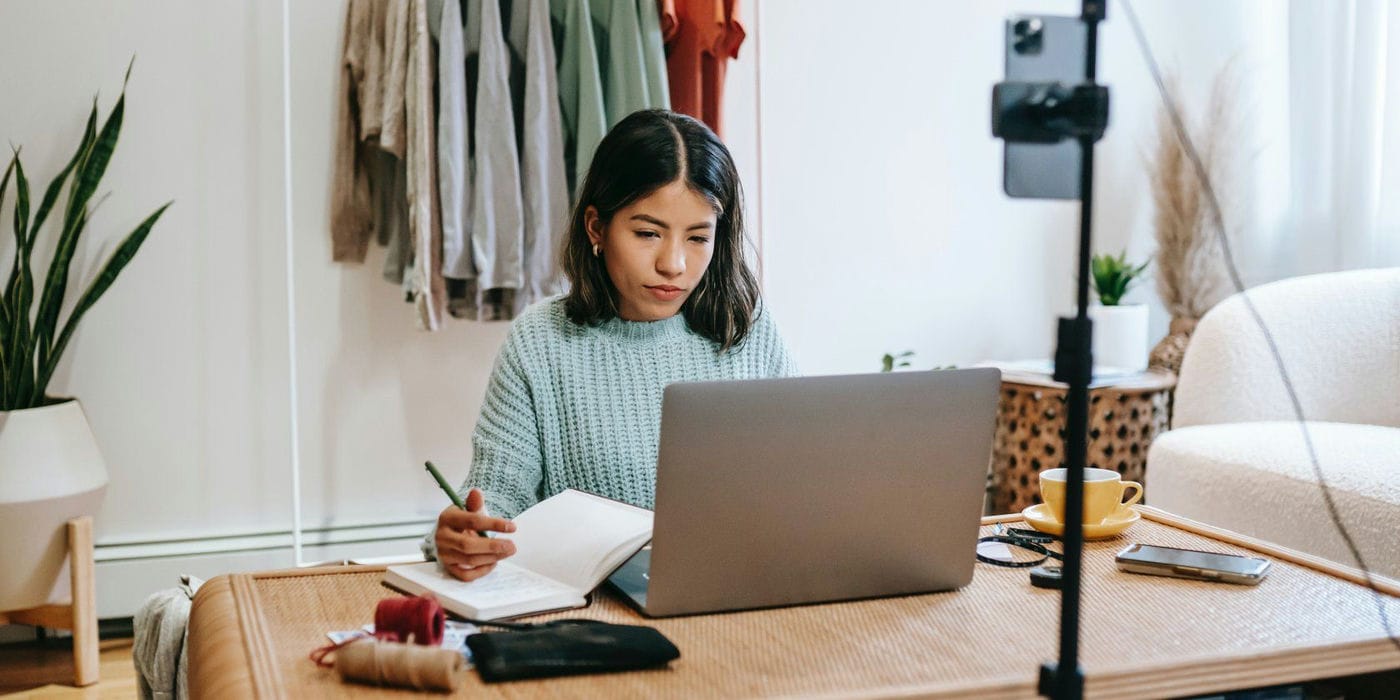 woman writing on desk with laptop in front of her